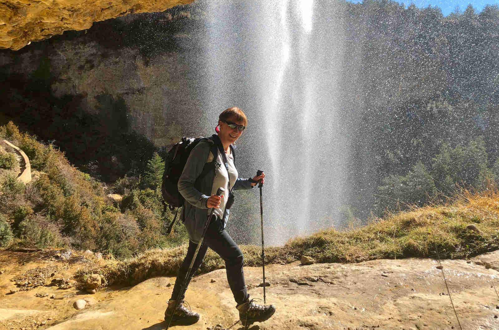 A hiker winter walking and passing behind a waterfall in beautiful sunshine on our Snowshoeing Holiday Spain with Aragon Active small group holidays