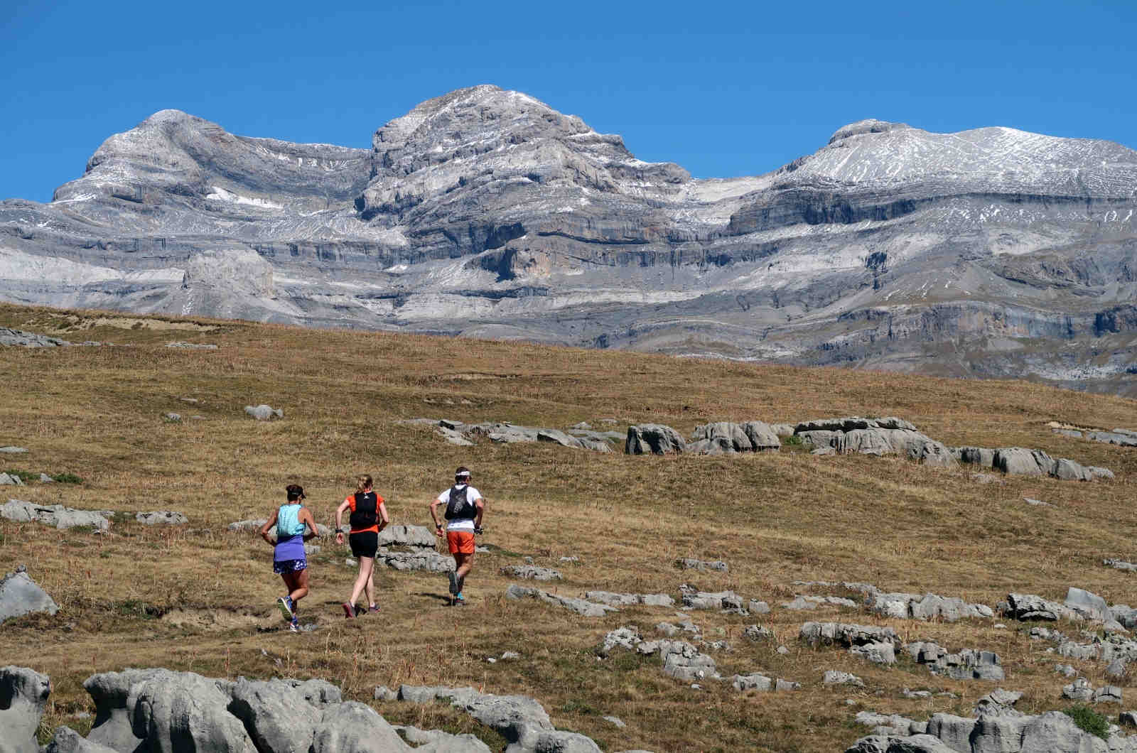 Three trail runners running up hill with the Three Marias mountains in the foreground in the Pyrenees on our Trail Running Holidays with Aragon Active small group holidays
