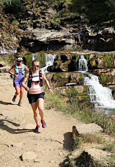 Two trail runners running down a track by waterfalls on our trail running holiday in the Spanish Pyrenees on Activity Holidays in Spain with Aragon Active
